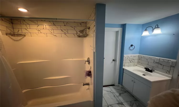 Bathroom featuring vanity, tile walls, marble finish floor, and  shower combination