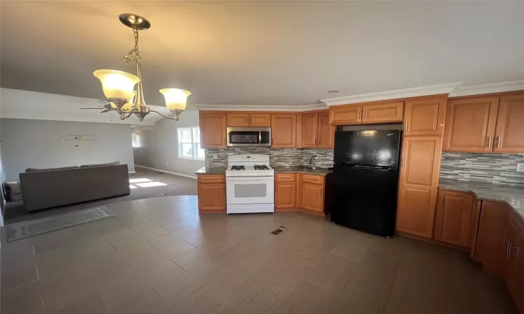 Kitchen featuring backsplash, stainless steel microwave, white range with gas stovetop, and freestanding refrigerator