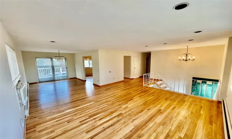 Unfurnished room featuring a notable chandelier, baseboards, light wood-type flooring, and baseboard heating