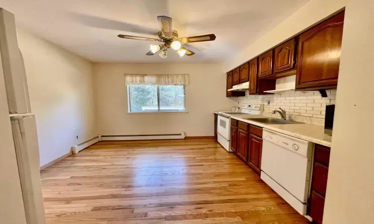 Kitchen featuring white appliances, a sink, light countertops, light wood-style floors, and under cabinet range hood