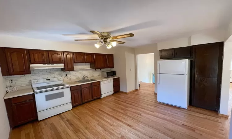 Kitchen with light wood finished floors, under cabinet range hood, light countertops, white appliances, and a sink