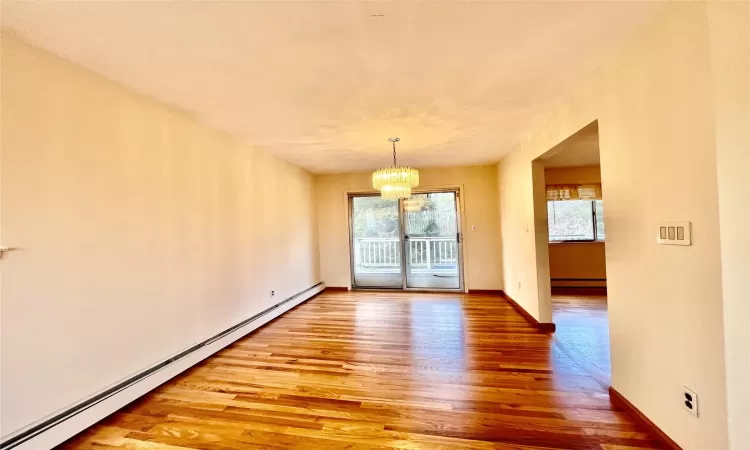 Unfurnished dining area with a notable chandelier, light wood-style flooring, a baseboard heating unit, and baseboards