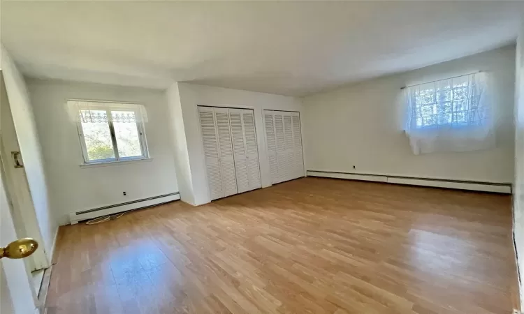 Unfurnished bedroom with multiple closets, baseboard heating, and light wood finished floors