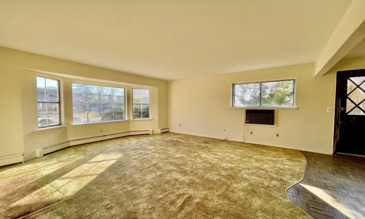 Unfurnished living room with a baseboard heating unit, plenty of natural light, and baseboards