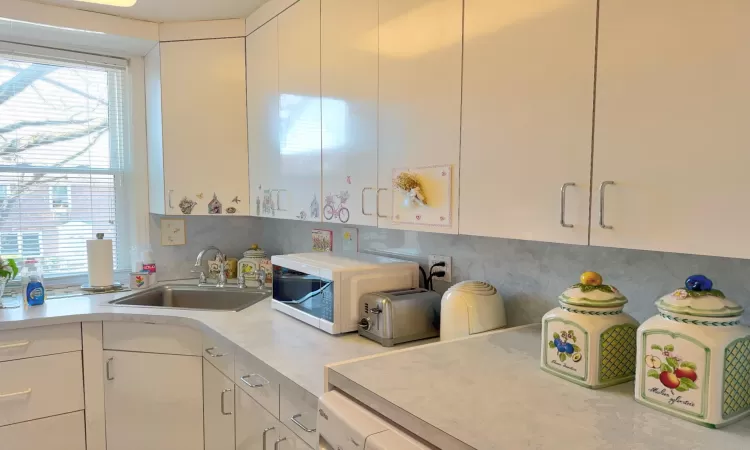 Kitchen with backsplash, white cabinets, light countertops, and a sink