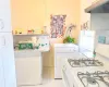 Kitchen with white gas stove, under cabinet range hood, light countertops, washer / dryer, and marble finish floor