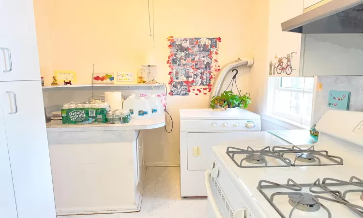 Kitchen with white gas stove, under cabinet range hood, light countertops, washer / dryer, and marble finish floor