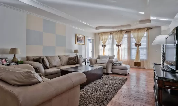 Living area featuring a tray ceiling, light wood-style flooring, and ornamental molding