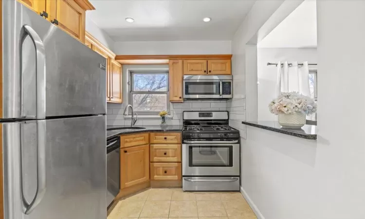 Kitchen with tasteful backsplash, dark stone counters, light tile patterned floors, appliances with stainless steel finishes, and a sink