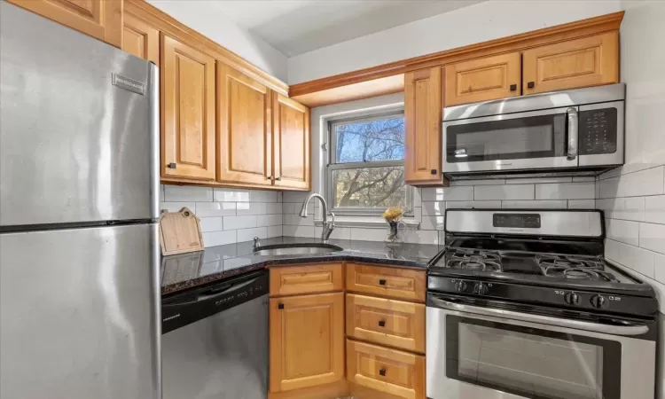 Kitchen featuring a sink, tasteful backsplash, appliances with stainless steel finishes, and dark stone countertops