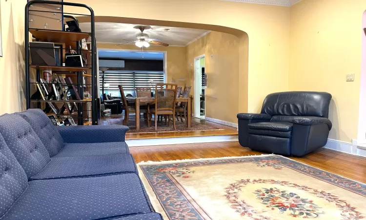 Living room with crown molding, baseboards, wood finished floors, arched walkways, and a ceiling fan