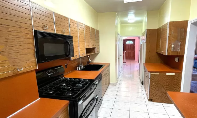 Kitchen featuring brown cabinetry, light tile patterned floors, black appliances, and a sink