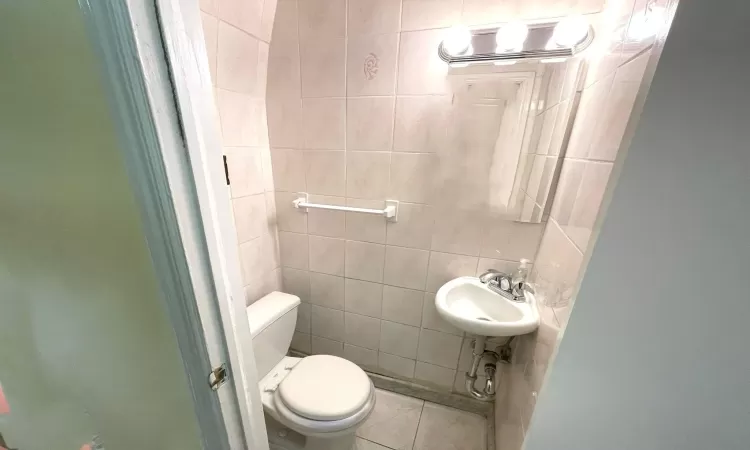 Bathroom featuring toilet, tile walls, and a sink