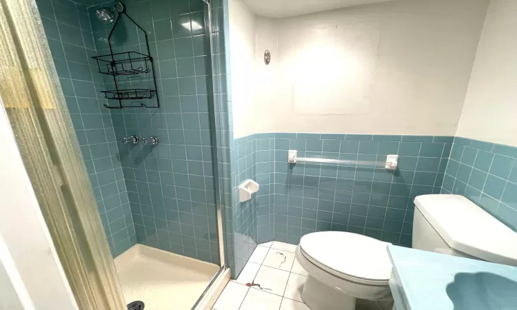 Bathroom featuring a shower stall, wainscoting, tile walls, toilet, and tile patterned floors