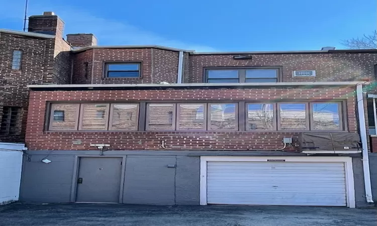 Back of property featuring driveway, brick siding, and an attached garage