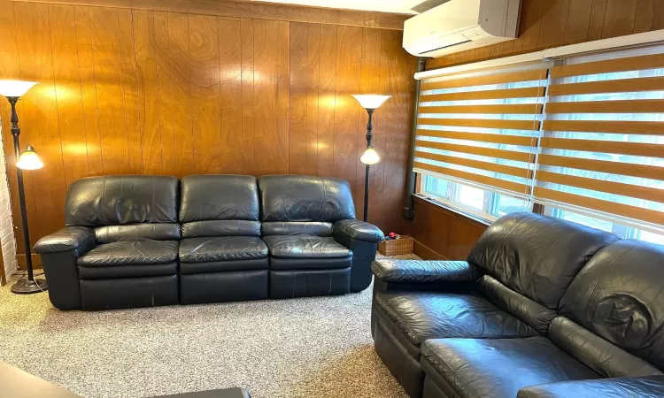 Carpeted living room featuring an AC wall unit and wooden walls