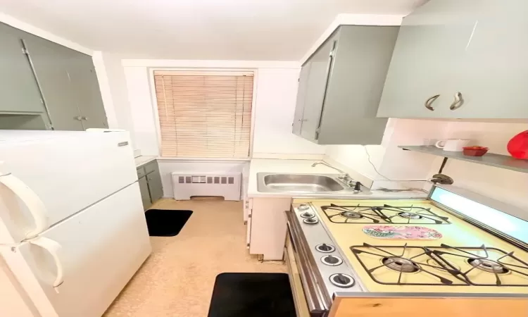 Kitchen with radiator heating unit, freestanding refrigerator, gray cabinetry, a sink, and range with gas cooktop