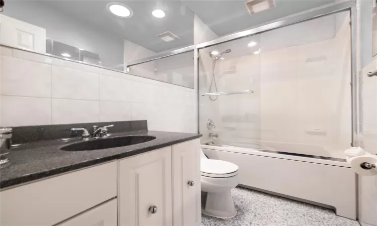 Bathroom with vanity, shower / bath combination with glass door, recessed lighting, tile walls, and toilet