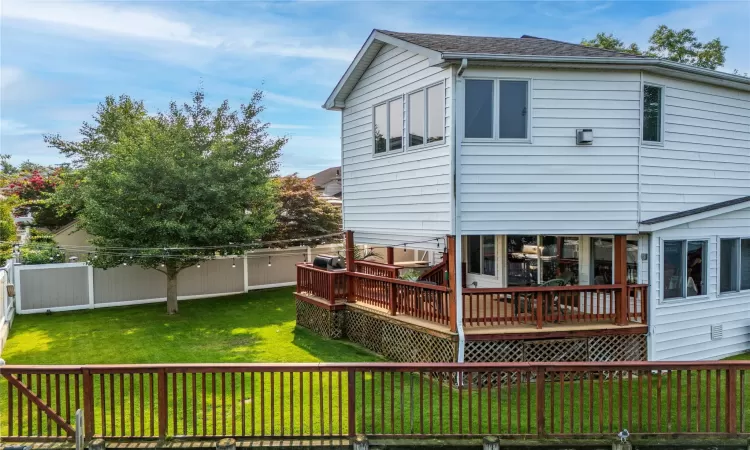 Rear view of house with a shingled roof, a fenced backyard, a lawn, and a wooden deck