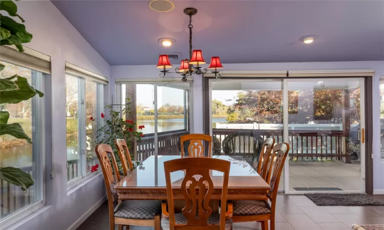 Dining area featuring baseboards, visible vents, vaulted ceiling, a water view, and a notable chandelier