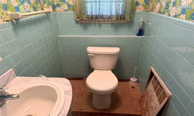 Bathroom featuring wallpapered walls, toilet, a sink, and wainscoting