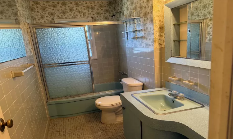 Full bathroom featuring toilet, tile walls, tile patterned flooring, enclosed tub / shower combo, and vanity