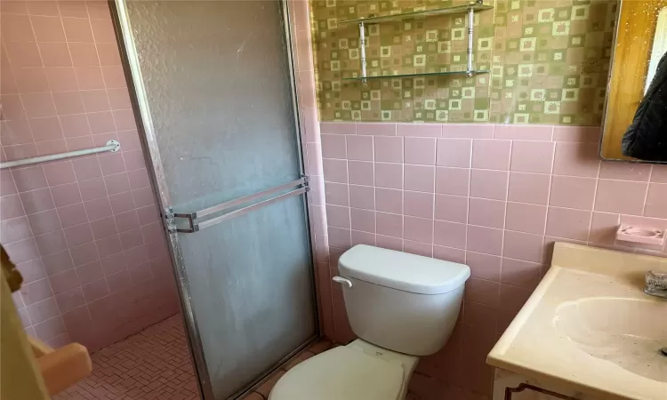 Bathroom featuring vanity, a wainscoted wall, a shower stall, tile walls, and toilet