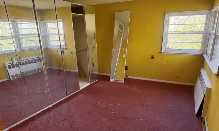 Unfurnished bedroom featuring radiator, multiple windows, carpet, and baseboards