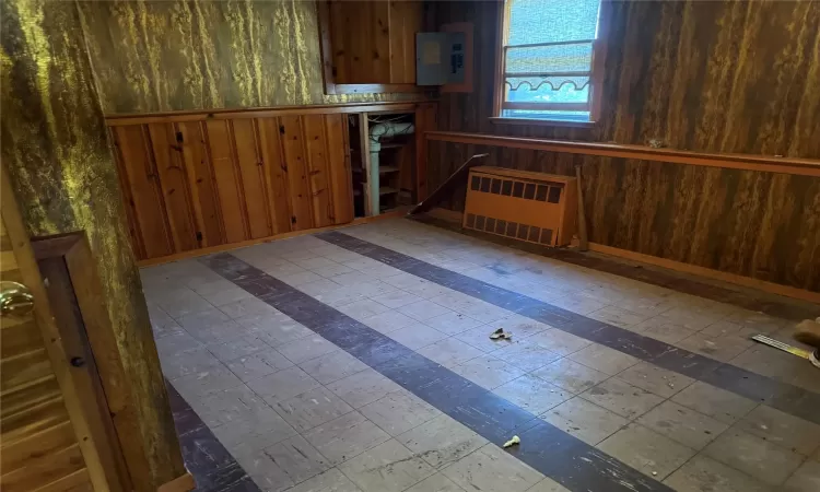 Kitchen with electric panel, wooden walls, and radiator heating unit