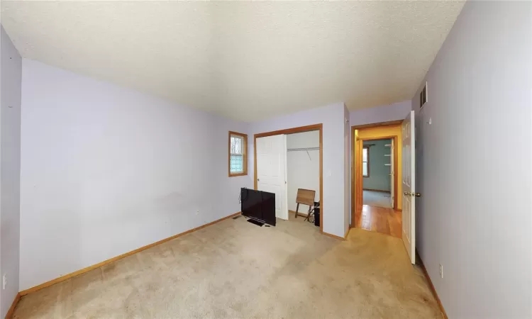 Unfurnished bedroom with baseboards, visible vents, a closet, a textured ceiling, and light colored carpet