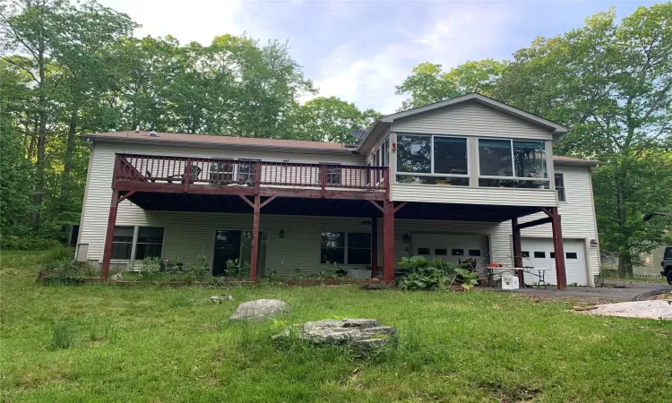 Rear view of house with a deck, a yard, a garage, and a sunroom