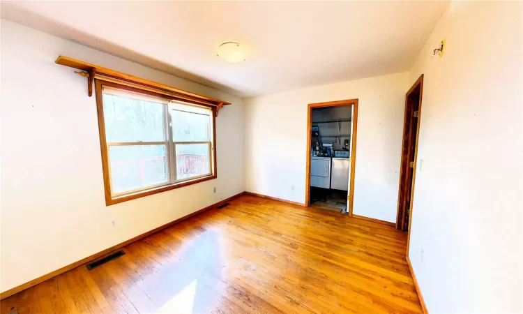 Empty room with washer and dryer, light wood-style flooring, baseboards, and visible vents