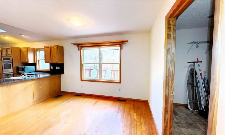 Kitchen featuring baseboards, light wood-type flooring, appliances with stainless steel finishes, dark countertops, and brown cabinets