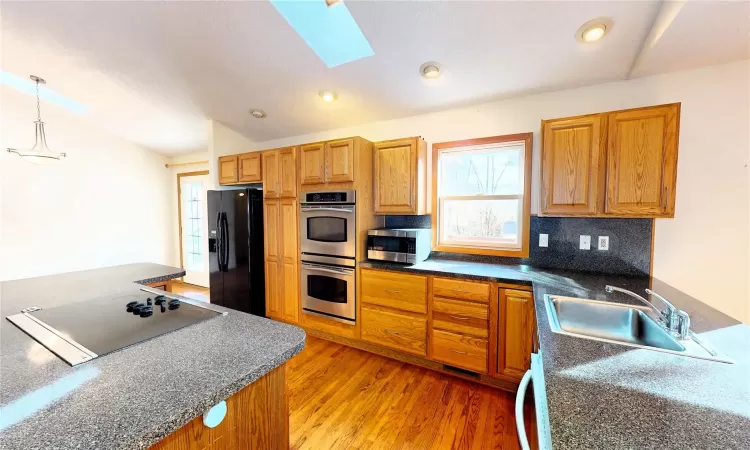 Kitchen with light wood-style flooring, a sink, black appliances, dark countertops, and tasteful backsplash