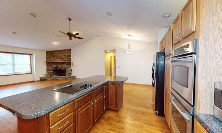 Kitchen featuring dark countertops, light wood-type flooring, lofted ceiling, a stone fireplace, and black appliances