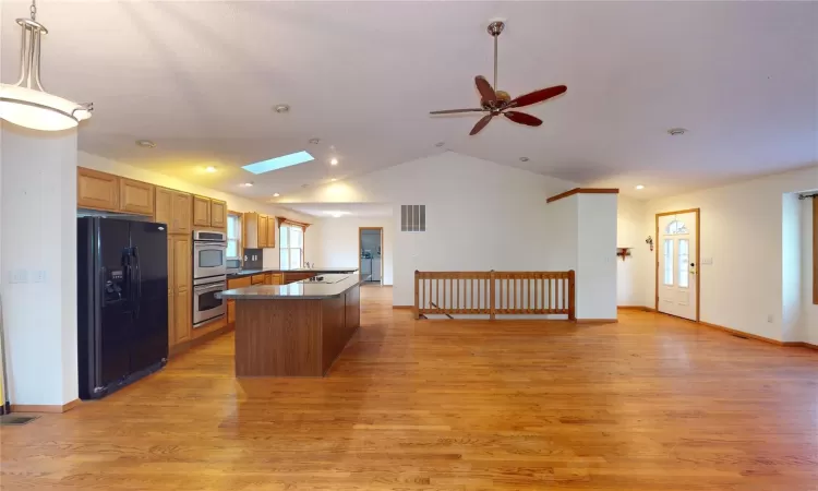 Kitchen featuring visible vents, light wood-style flooring, black fridge with ice dispenser, dark countertops, and double oven