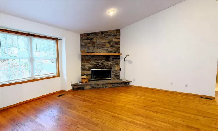 Unfurnished living room with visible vents, lofted ceiling, wood finished floors, a stone fireplace, and baseboards