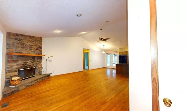 Unfurnished living room with visible vents, light wood-style flooring, ceiling fan, a stone fireplace, and vaulted ceiling