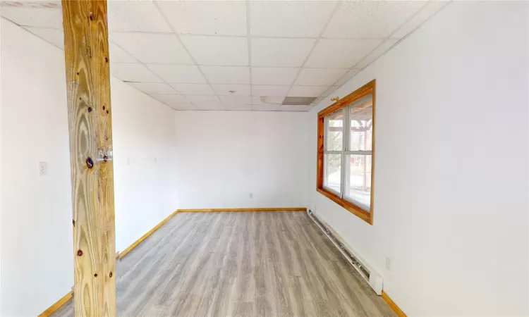 Empty room with a baseboard heating unit, wood finished floors, a paneled ceiling, and baseboards