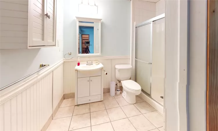 Bathroom featuring tile patterned floors, toilet, a wainscoted wall, and a stall shower