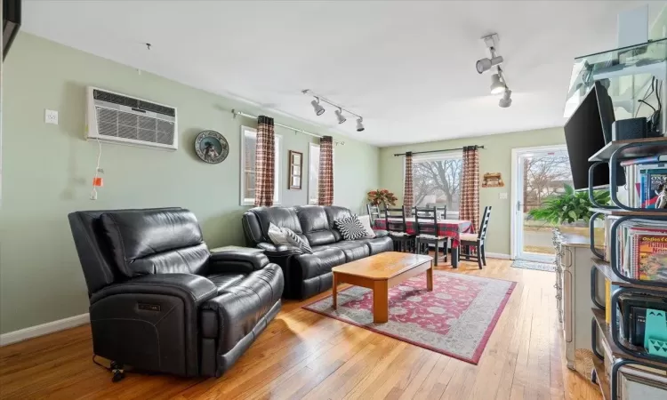 Living area featuring an AC wall unit, hardwood / wood-style flooring, baseboards, and track lighting