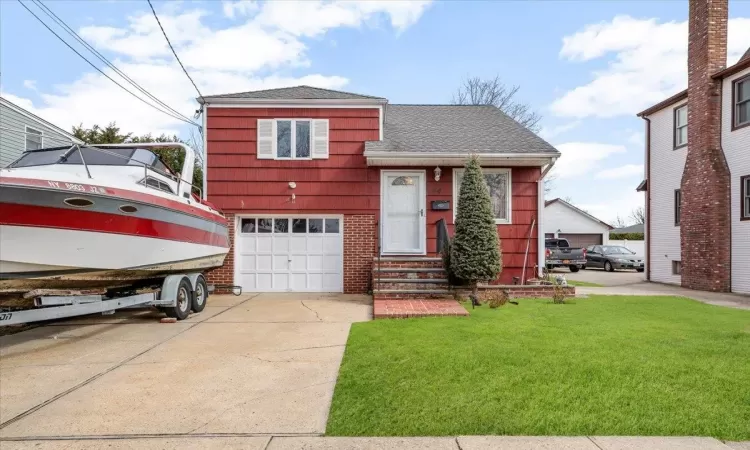 Split level home with roof with shingles, concrete driveway, a front yard, a garage, and brick siding