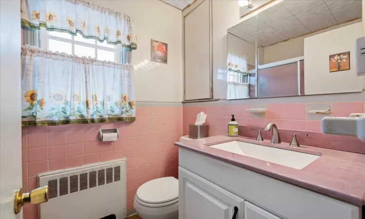 Bathroom featuring vanity, radiator, wainscoting, tile walls, and toilet