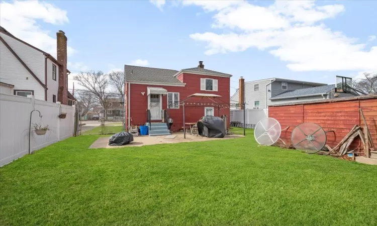 Back of house featuring entry steps, a fenced backyard, a lawn, and a chimney