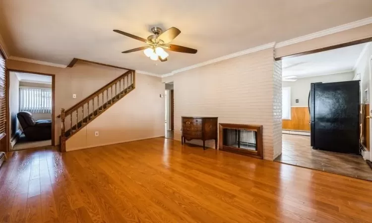 Unfurnished living room with a brick fireplace, crown molding, a baseboard heating unit, stairs, and hardwood / wood-style floors