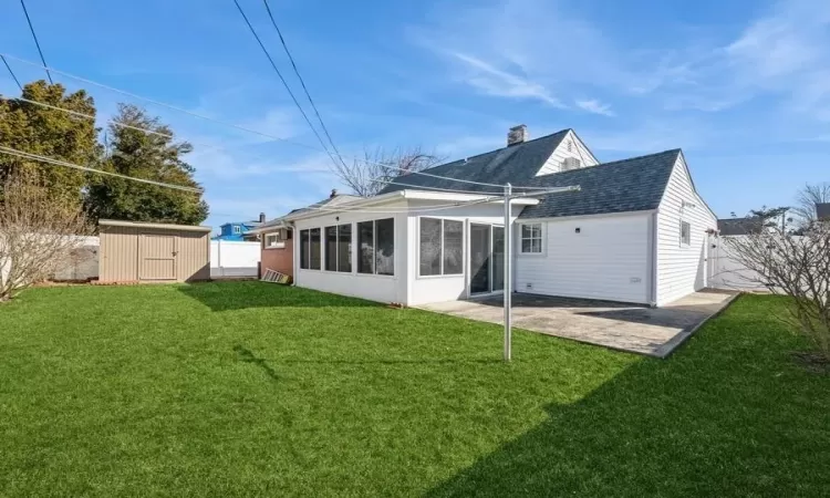 Back of property featuring a storage shed, a fenced backyard, a chimney, and a sunroom