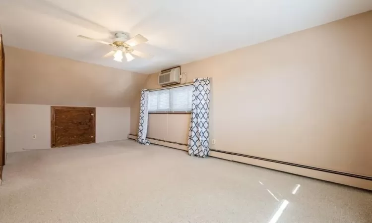 Bonus room featuring a wall unit AC, a baseboard radiator, light colored carpet, ceiling fan, and vaulted ceiling