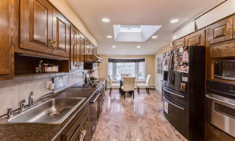 Kitchen with lofted ceiling with skylight, black appliances, a sink, tasteful backsplash, and recessed lighting