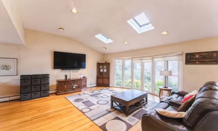 Living room featuring a baseboard heating unit, lofted ceiling with skylight, recessed lighting, wood finished floors, and a baseboard radiator