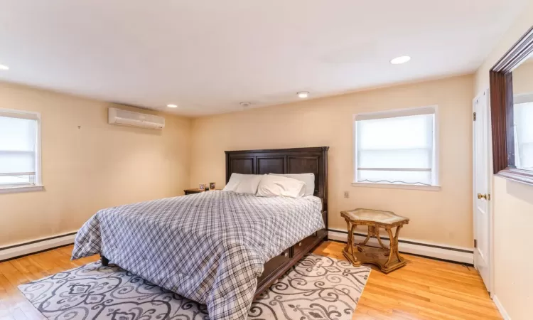 Bedroom with a baseboard heating unit, an AC wall unit, and light wood finished floors